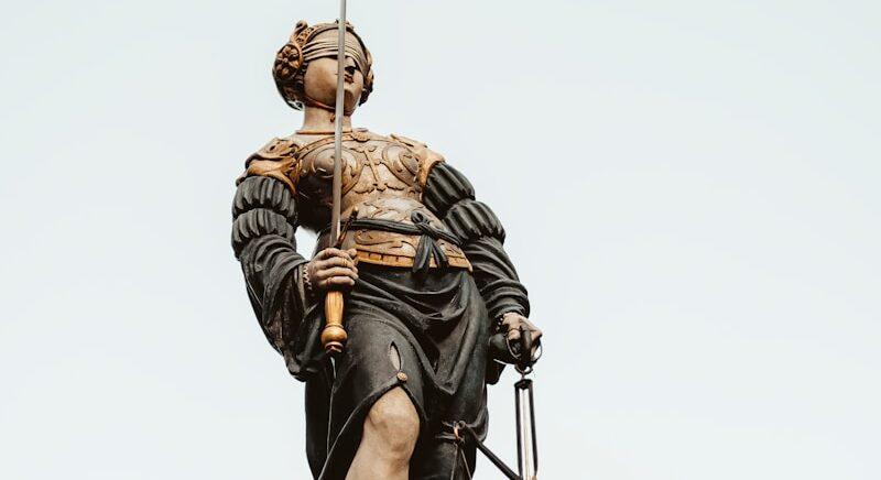 woman holding sword and balance scale statue under white sky