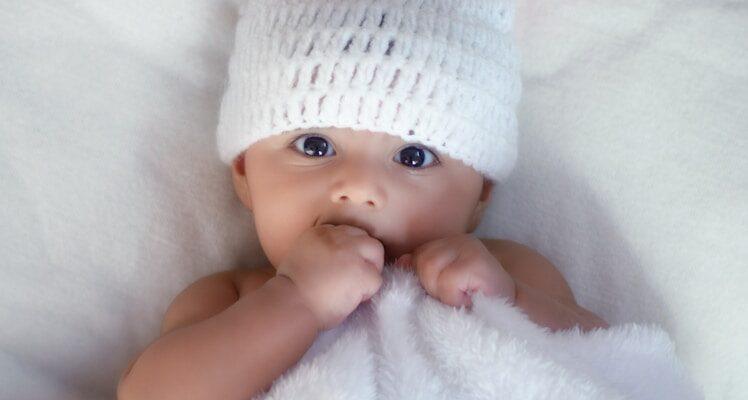 baby in white knit cap lying on white textile